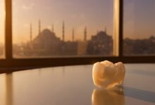 A close-up, photorealistic image of a perfect white dental crown on a reflective surface, with the beautiful, out-of-focus skyline of Istanbul, Turkey, visible behind it during a warm sunset.
