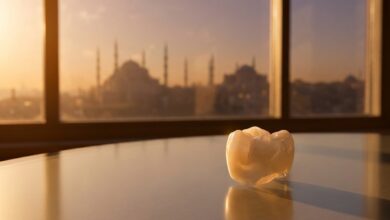A close-up, photorealistic image of a perfect white dental crown on a reflective surface, with the beautiful, out-of-focus skyline of Istanbul, Turkey, visible behind it during a warm sunset.