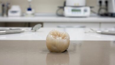 A close-up, photorealistic image of a single, perfectly crafted ceramic dental implant crown sitting in a clean, modern, and brightly lit setting. The focus is sharp on the crown, revealing its natural texture and color, while the background is softly blurred.