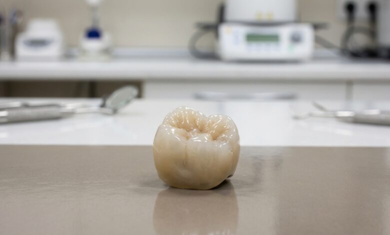 A close-up, photorealistic image of a single, perfectly crafted ceramic dental implant crown sitting in a clean, modern, and brightly lit setting. The focus is sharp on the crown, revealing its natural texture and color, while the background is softly blurred.