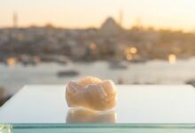 A photorealistic close-up of a flawless Zirconia dental crown on a clean surface, with the blurred skyline of Istanbul, Turkey in the background during a warm sunrise, symbolizing high-quality dental tourism.