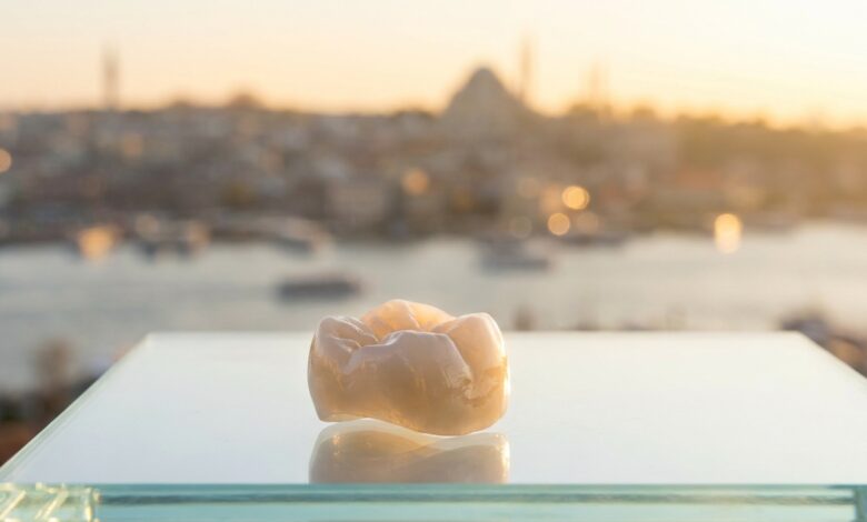 A photorealistic close-up of a flawless Zirconia dental crown on a clean surface, with the blurred skyline of Istanbul, Turkey in the background during a warm sunrise, symbolizing high-quality dental tourism.