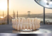 A photorealistic image of a full-arch Zirconia dental implant bridge on a clean surface in a modern dental clinic, with a blurred view of Istanbul, Turkey, visible through a window in the background.