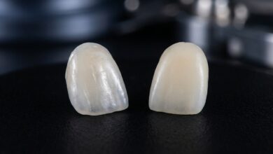 A close-up, photorealistic image showing two different types of dental veneers side-by-side for comparison. The porcelain veneer on the left is translucent and mimics natural enamel, while the composite veneer on the right is more opaque.