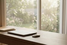 A photorealistic shot of a modern office desk with a laptop next to a large window. The view outside is a peaceful, blurred garden, symbolizing a calm return to work after a period of recovery. The lighting is soft and natural.
