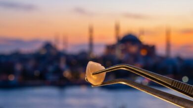 A close-up, photorealistic image of a perfect white zirconia dental crown held by tweezers, with the sun setting over a heavily blurred background of the Istanbul, Turkey skyline and the Bosphorus.