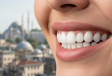 Close-up of a person smiling, showing a perfect set of white, even teeth that represent dental veneers. The background is softly blurred, revealing a generic Turkish cityscape with architectural elements like domes or minarets under a bright sky.