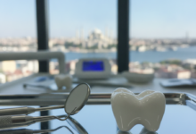 A close-up of a pristine, white ceramic dental crown on a sterile surface with blurred dental tools. In the background, a softly focused cityscape of Istanbul, Turkey, under a clear sky.