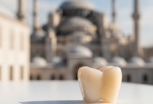 Close-up of a meticulously crafted, natural-looking ceramic dental crown against a softly blurred background featuring a distinct, warm-toned silhouette of an iconic Turkish mosque or historical building under bright daylight. The crown is the sharp focal point.