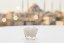 A pristine, perfectly white dental crown displayed on a clean surface in the foreground, with the iconic, blurred skyline of Istanbul, Turkey, featuring minarets and domes, visible in the background, symbolizing high-quality dental tourism.