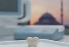 A perfectly crafted, luminous dental crown in sharp focus, showcasing its natural translucency and smooth surface. The background is softly blurred, hinting at a modern dental clinic setting, with a very distant, indistinct silhouette of a Turkish landmark under a warm sky.