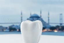 Close-up of a perfectly white, flawless dental crown on a clean, subtly reflective surface. In the soft-focus background, a blurred silhouette of an iconic Turkish landmark is visible, symbolizing dental tourism and advanced dental care.