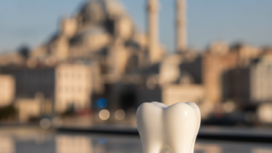 A close-up, photorealistic image of a sparkling white dental crown resting on a polished, sterile-looking surface. The background is softly blurred, showing a warm Turkish cityscape with a distinct dome and a minaret under a bright sky, suggesting dental tourism in Turkey.