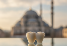 A close-up, photorealistic image of a perfectly crafted, natural-looking white dental crown resting on a sterile, reflective surface. In the heavily blurred background, the distinct silhouette of a mosque dome and minaret against a bright sky subtly indicates Turkey, emphasizing high-quality dental tourism.