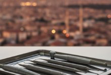 A close-up, photorealistic image of sterile, gleaming dental instruments neatly arranged on a modern, reflective surface in a professional dental clinic. The background features a softly blurred, generic cityscape of Turkey at dusk, suggesting dental tourism and high-quality care.