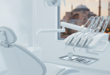 A modern, sterile dental clinic interior with a sleek, empty dental chair and high-tech dental instruments on a tray in the foreground. Through a large, blurred window in the background, a recognizable, out-of-focus Turkish landmark like the Hagia Sophia or a mosque's minaret, overlooking the Bosphorus, is visible. The lighting is bright and cinematic, emphasizing cleanliness and the fusion of dental care with tourism. No text or visible branding.